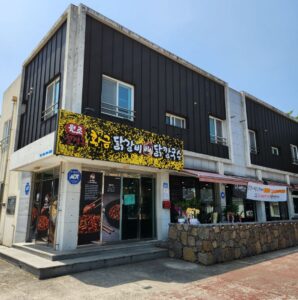 제주 황금닭갈비 이도점, 제주시 이도이동 남광로의 검은 외벽 건물 1층에 걸린 「원조칠성 황금 닭갈비 닭칼국수」 간판과 돌담 위 화분